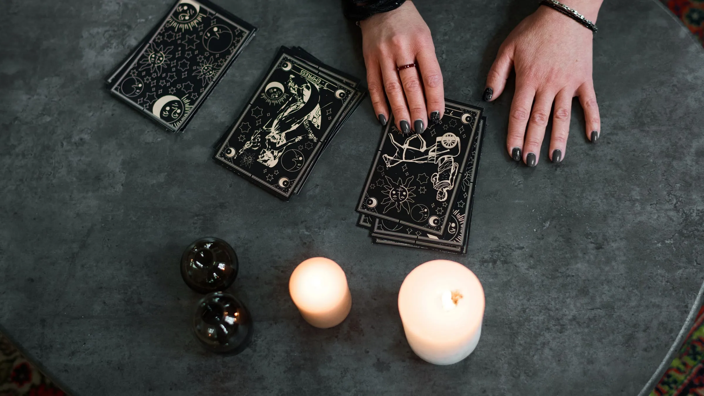 A psychic soulmate drawing session: tarot cards, two lit candles and a reader's hands on a dark stone table