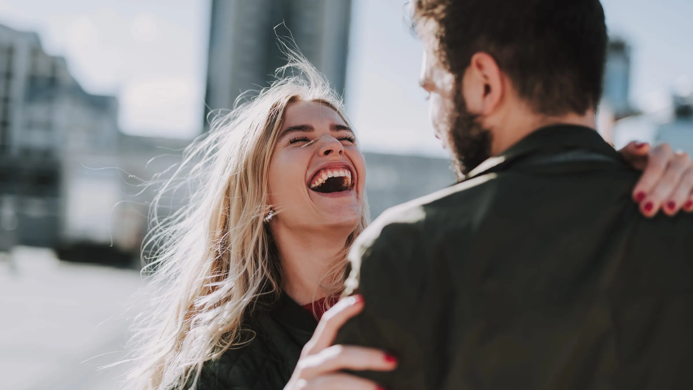 Types of soulmates: a woman laughing as she holds on to a man's shoulders outdoors