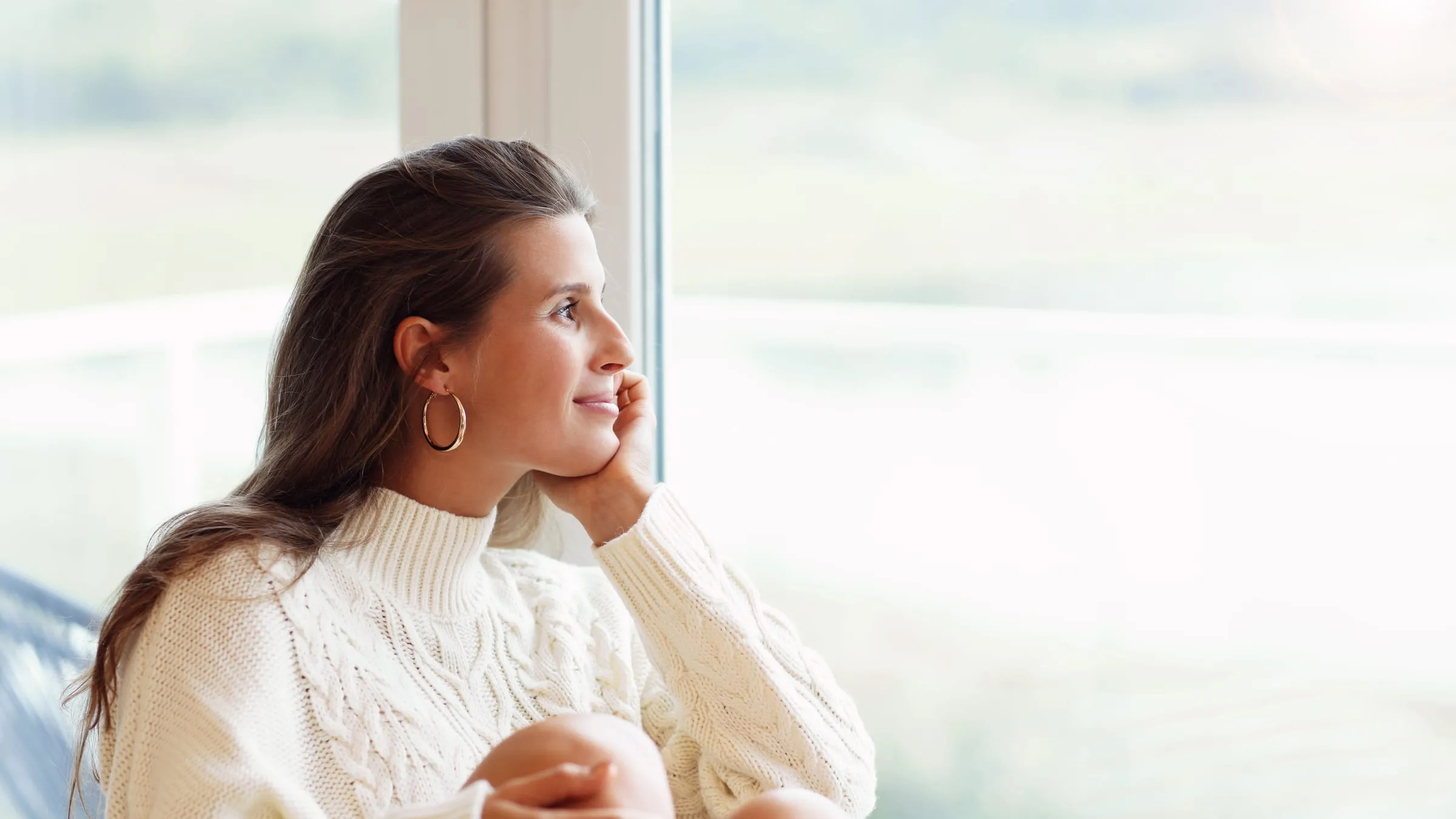 What does my future husband look like? A woman in a cream sweater daydreams at a bright window